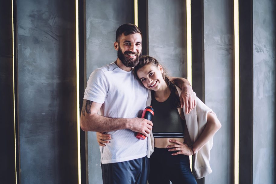 Satisfied athletic couple standing near wall in embrace
